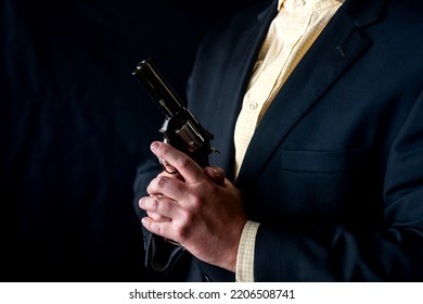 One Male Spy In A Professional Tuxedo Holds A Revolver Pistol Before The Start Of A Film Shoot. Portrait Silhouette In The Studio. Isolated Black Background. Male Actor With A Gun