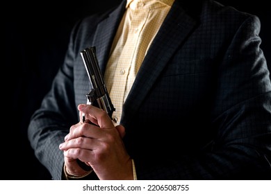 One Male Spy In A Professional Tuxedo Holds A Revolver Pistol Before The Start Of A Film Shoot. Portrait Silhouette In The Studio. Isolated Black Background. Male Actor With A Gun