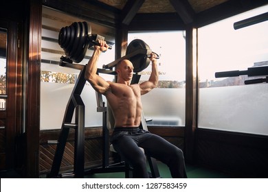 One Man, 30-39 Years, Bodybuilder Exercising Overhead Plate Press Machine. At Home (with Many Windows) In His Own Gym With Professional Fitness Equipment.