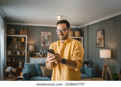 One man adult caucasian male with beard and eyeglasses stand at home happy smile use mobile phone smartphone to send sms text messages or browse internet online copy space - Powered by Shutterstock