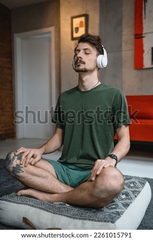 one man adult caucasian male on the floor use headphones for online guided meditation practicing mindfulness yoga with eyes closed at home real people self care manifestation concept copy space