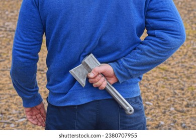 one man in blue clothes hides his hand with a gray small ax behind his back on the street