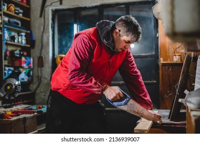 One Man Carpenter Working At His Garage Workshop Hobby And Craft Concept Using Hand Saw To Cut Wood Plank