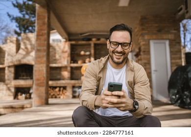 One man caucasian male with beard and eyeglasses sit outdoor in sunny day wear shirt use mobile smart phone for sms text messages browse internet online or video call use app copy space real people - Powered by Shutterstock