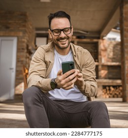 One man caucasian male with beard and eyeglasses sit outdoor in sunny day wear shirt use mobile smart phone for sms text messages browse internet online or video call use app copy space real people - Powered by Shutterstock