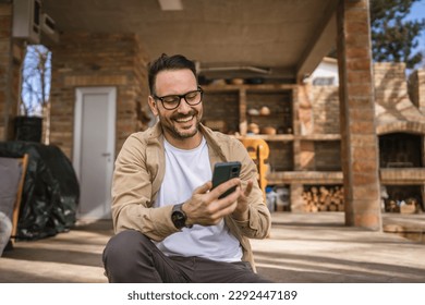 One man caucasian male with beard and eyeglasses sit outdoor in sunny day wear shirt use mobile smart phone for sms text messages browse internet online or video call use app copy space real people - Powered by Shutterstock