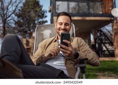 One man caucasian male with beard and eyeglasses sit outdoor in sunny day wear shirt use mobile smart phone for sms text messages browse internet online or video call use app copy space real people