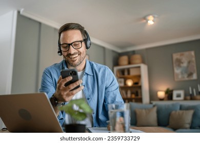 One man caucasian male freelancer work from home with headphones on his head use mobile phone and laptop computer customer support dispatcher - Powered by Shutterstock