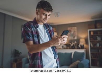 One man caucasian male teenager boy use smartphone mobile phone for online internet browsing social network or sms text messages at home happy smile - Powered by Shutterstock