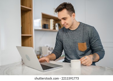 One Man Caucasian Young Adult Male In The Kitchen In The Morning Working On The Laptop Computer With Cup Of Coffee Daily Routine Internet Browsing Online Search Real People Copy Space