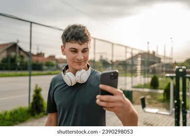 One man caucasian young male stand at outdoor open training park gym use mobile phone smartphone with headphones send messages texting or browse internet online app for training real person copy space - Powered by Shutterstock