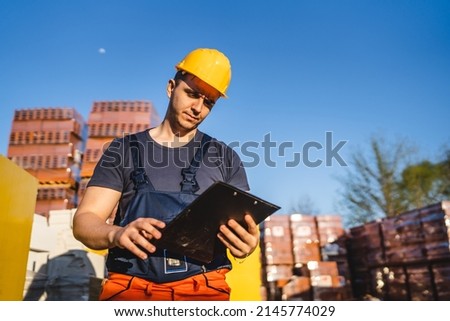 One man construction worker standing at warehouse or on the site holding clip document checking supply building material wearing protective helmet making inspection and control copy space