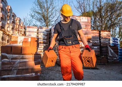One man construction worker taking and carry or hold clay orange hollow blocks ar warehouse or construction site in sunny summer day copy space - Shutterstock ID 2179439987
