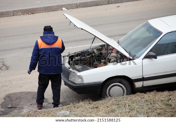 One\
man fixing car engine under the open bonnet of a old European\
vehicle on road, cold engine start and repair\
outdoor