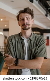 One Man Front View Portrait Waist Up Standing Indoor In Cafe Or Restaurant Lobby Happy Smile Confident Wear Olive Shirt With Modern Haircut Mustaches And Beard Looking To The Camera