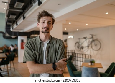 One Man Front View Portrait Waist Up Standing Indoor In Cafe Or Restaurant Lobby Happy Smile Confident Wear Olive Shirt With Modern Haircut Mustaches And Beard Looking To The Camera