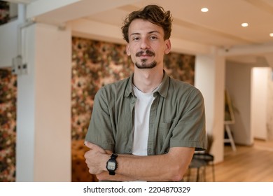 One Man Front View Portrait Waist Up Standing Indoor In Cafe Or Restaurant Lobby Happy Smile Confident Wear Olive Shirt With Modern Haircut Mustaches And Beard Looking To The Camera