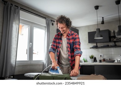 one man ironing clothes at home hold iron on shirt on board household chores concept adult male in 30s living in the apartment alone doing housework copy space