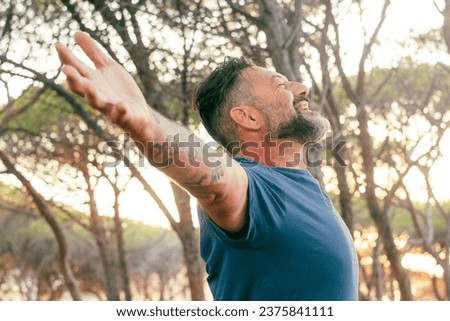 One man outstretching arms in front of a high trees forest and sunset sunlight. Concept of environment and healthy lifestyle. People and love for nature. Male opening arms in front of sun. Travel day