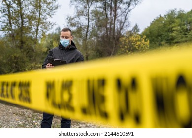 One man police detective or inspector securing crime scene using radio for communication waiting for back up during investigating procedure collecting evidence near the river in day nature copy space