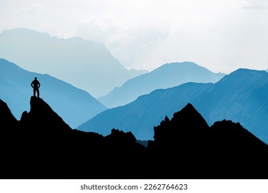 One Man reaching summit after climbing and hiking enjoying freedom and looking towards mountains silhouettes panorama during sunrise. - Powered by Shutterstock