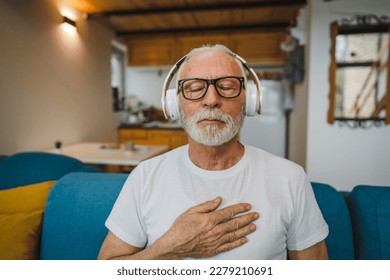 One man senior caucasian male eyes closed for guided training yoga or meditation while sitting at home with headphones self-care practice real people well-being inner peace and balance concept - Powered by Shutterstock