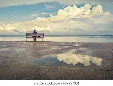 One man sitting on a bench on the beach with beautiful clouds in the background.  - Powered by Shutterstock