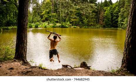 One Man Swinging From A Rope Into A Forest Lake On A Cloudy Day. Taken In Dentlein Am Forst, In Bavaria, Germany.