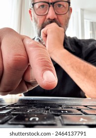 One man using laptop and looking at display with doubts thoughtful expression. Concept of security and privacy online in scam fraud website. Finger in closeup and man in background. Remote working
