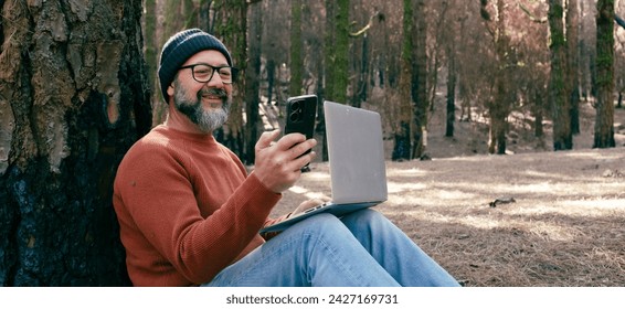 One man using phone cellular connection in a forest wood enjoying technology and outdoor leisure activity. Modern man speaking at cellular with trees in background. People and communication on travel