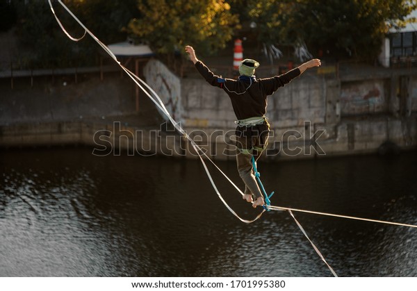 one man walk and balanced on stretched\
sling. Water and bank of river in\
background.