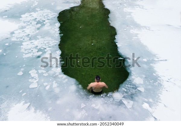 One man in water hole of\
icy water covered with white snow and ice practicing cold water\
therapy, 