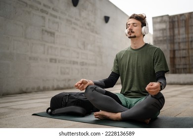 One man young adult caucasian male eyes closed for guided training yoga or meditation while sitting outdoor with headphones self-care practice real people well-being inner peace and balance concept - Shutterstock ID 2228136589