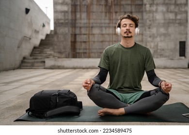 One man young adult caucasian male eyes closed for guided training yoga or meditation while sitting outdoor with headphones self-care practice real people well-being inner peace and balance concept - Powered by Shutterstock