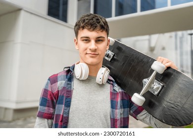 One man young adult caucasian teenager stand outdoor with skateboard on his shoulder and headphones posing portrait looking to the camera happy confident wear shirt casual real person copy space - Powered by Shutterstock