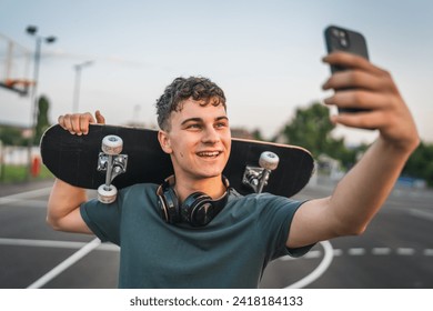 One man young adult caucasian teenager stand outdoor with skateboard on his shoulder and headphones posing at basketball court portrait happy confident wear shirt casual real person copy space - Powered by Shutterstock