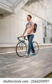 One Man Young Adult Male With Brown Hair And Mustaches Walking By The Building With Rucksack On His Back And Bicycle Happy Smile Joyful Real People Copy Space Side View Full Length