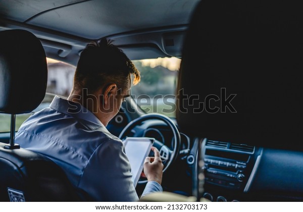 One man young adult manager or sales director\
business person sitting on the front seat of car using digital\
tablet to check road direction or order business details while\
waiting in the automobile