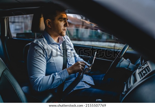One man young adult manager or sales director\
business person sitting on the front seat of car using digital\
tablet to check road direction or order business details while\
waiting in the automobile