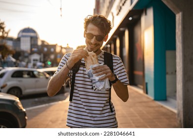 One man young adult modern caucasian male in the city in sunny day walk and eat sandwich fast food concept urban life copy space tourist eating on the street real person