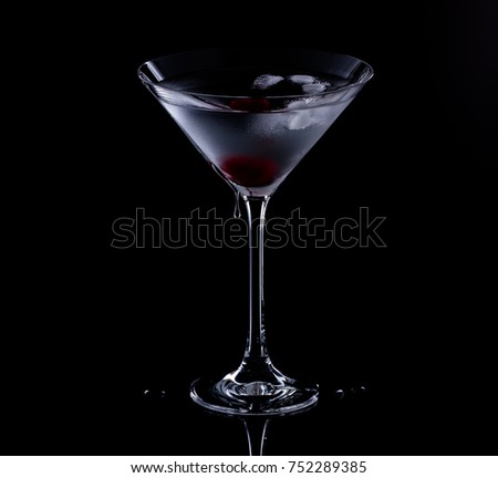 One martini glass filled with a cold, clear drink with a red cherry at the bottom of the glass. It is against a black background with a reflection.