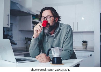 One Mature Man At Home Having A Coffe In The Morning In The Kitchen. Single People Lifestyle. Modern Adult Male Drinking Espresso From Traditional Italian Moka And Using Laptop Computer To Read News