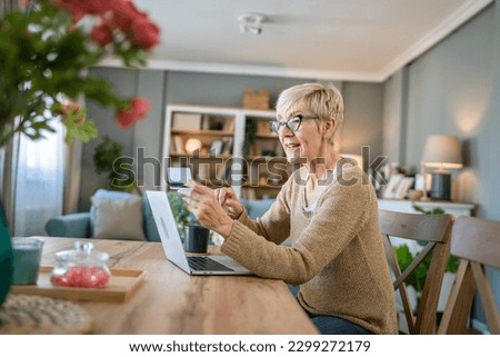 One mature senior woman grandmother sit at home use credit or debit card for online shopping browse internet stores use laptop computer buying stuff real people copy space
