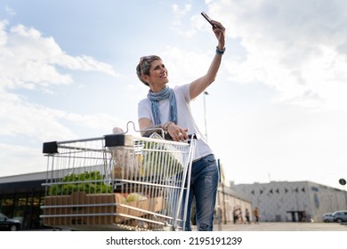 One Mature Woman Caucasian Female Walking In The Parking Lot In Front Of The Shopping Center Grocery Store Supermarket Chart Using Mobile Phone For Selfie Or Make A Video Call While Waiting Copy Space