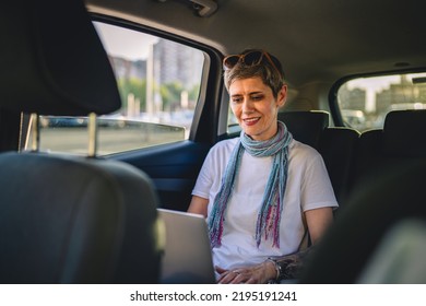 One Mature Woman Caucasian Female Sitting On The Back Seat Of The Car Working On Laptop Computer In Summer Day With Short Gray Hair Modern Manager Or Business Owner On Road Wearing Casual Copy Space