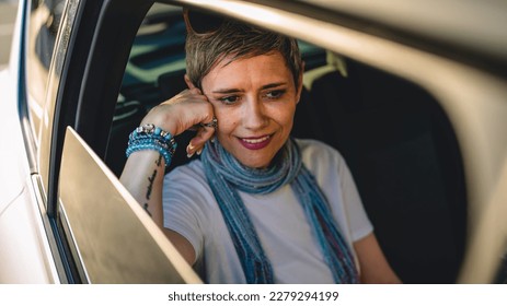 One mature woman caucasian female sitting on the back seat of the car looking trough the glass window in summer day happy smile travel and transport concept copy space real person gray short hair