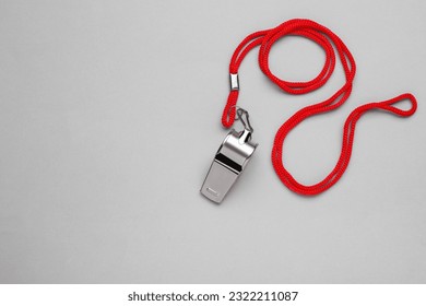 One metal whistle with red cord on light grey background, top view. Space for text