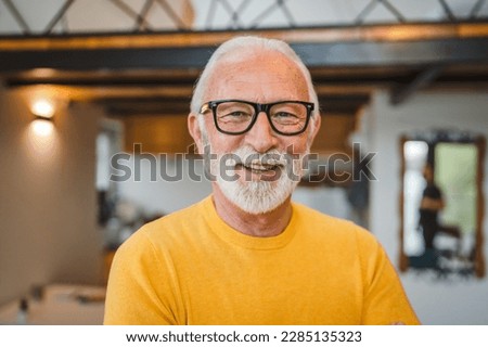 One modern senior caucasian man portrait of male grandfather with beard stand in his house in day wear yellow sweater happy confident copy space portrait