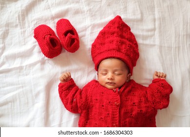 A One Month Old Baby Sleeping And Dressed In Red Woolen Clothing On White Muslin Cloth.