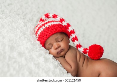 A one month old baby wearing a white and red, crocheted stocking cap. Photographed on a white, fluffy blanket.